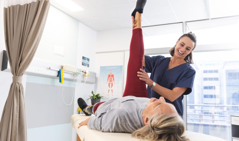 Caucasian female physiotherapist and senior woman with artificial leg stretching at hospital. Hospital, disability, physiotherapy, work, medicine and healthcare, unaltered.