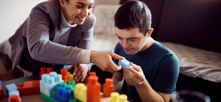 Happy psychologist and man who has down syndrome playing with toy blocks during home visit.
