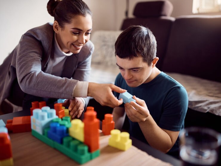 Happy psychologist and man who has down syndrome playing with toy blocks during home visit.