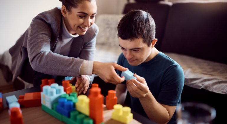 Happy psychologist and man who has down syndrome playing with toy blocks during home visit.