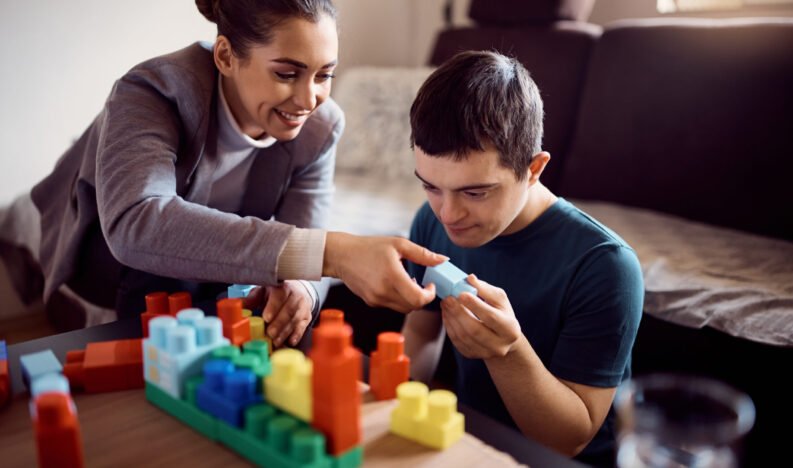 Happy psychologist and man who has down syndrome playing with toy blocks during home visit.