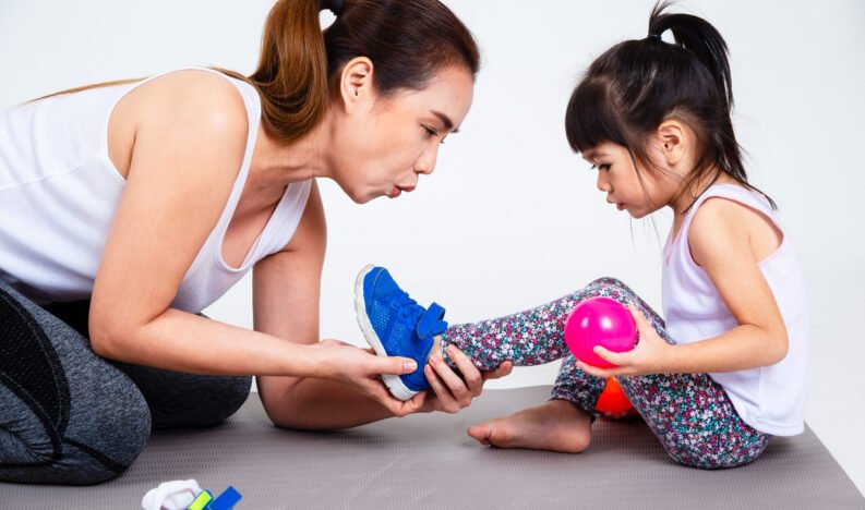 Young asian mother helping her lovely daughter wearing sport shoes before exercise on white background